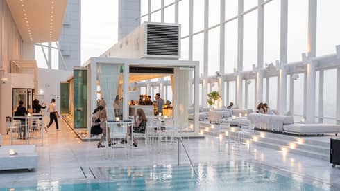 People mingle around a contemporary white bar next to pool