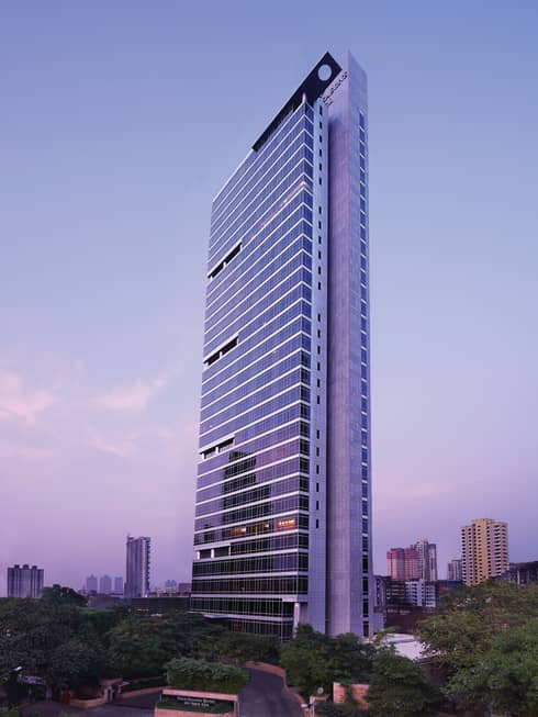 Four Seasons Hotel Mumbai glass tower exterior with trees around entrance, sign