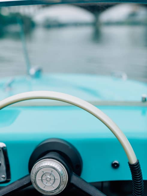 The steering wheel of an old boat with a bridge in the distance.