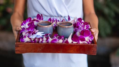A woman holds a tray of two bespoke ceramic cups and purple Hawaiian flowers
