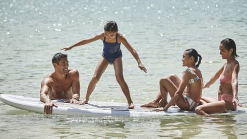A family sitting on a large surf or paddleboard.