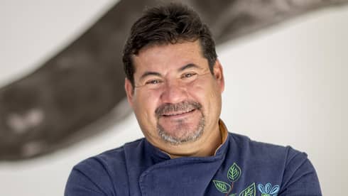 A chef wearing a navy embroidered coat with their arms crossed and smiling
