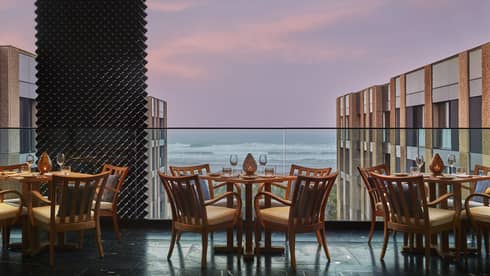 Patio dining tables on glass balcony overlooking ocean at sunset