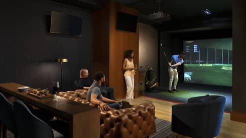 A group of people enjoying an indoor golf simulator experience at the luxury hotel Topgolf Swing Suite, with plush seating and a relaxed atmosphere