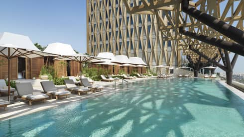 An olympic size pool surrounded by lounge chairs shaded by large white umbrellas