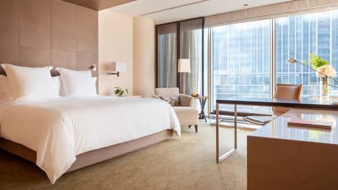 Guest room with large windows, city views, king bed, lamp, armchair and workspace