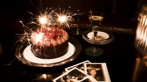 Sparkler candles in a chocolate cake and polaroid pictures nearby on a table