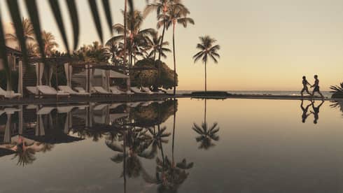 A reflective pool at a tropical resort with beach in the distance