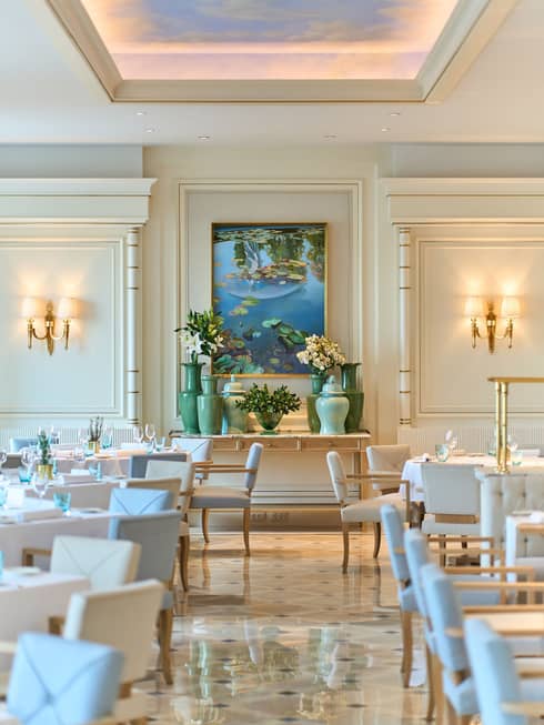 Brightly lit dining room of Riviera with lighted wall sconces, pale blue and white chairs, shiny patterned floor