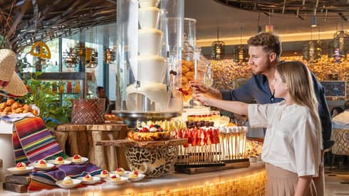 An adult and a child stand in front of a dessert buffet display