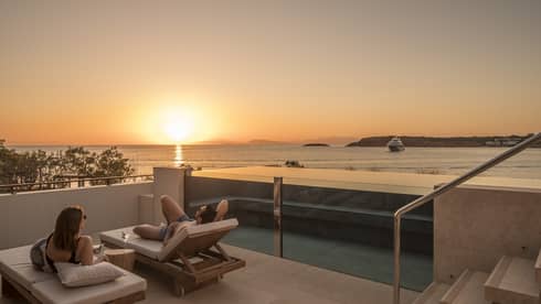 Couple relaxes on plush lounge chairs on Nafsika One Bedroom Terrace Suite with Pool deck