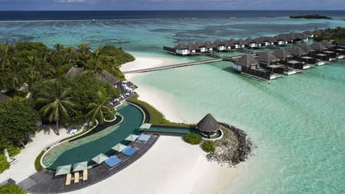 Aerial view of resort with villas over water and coast with white sands and palm trees