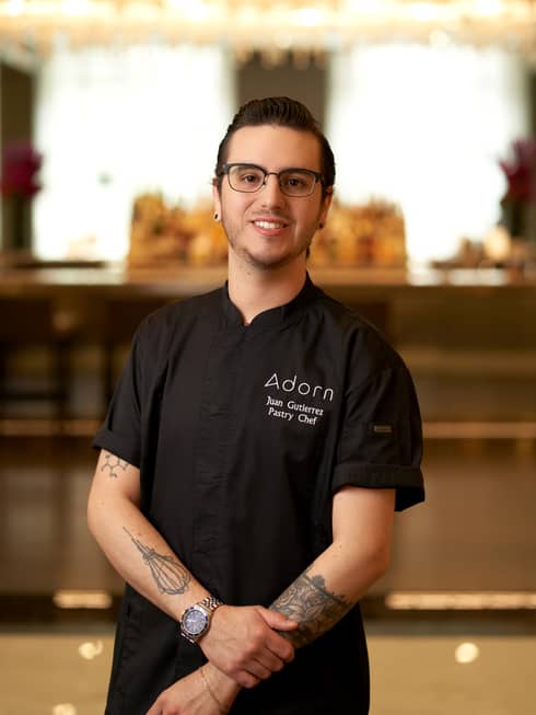 A young male chef in black chef clothes and glasses.