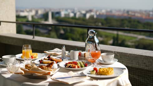 Sunny balcony breakfast dining table with fresh fruit plates, juice, coffee 