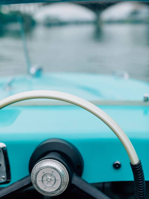 The steering wheel of an old boat with a bridge in the distance.
