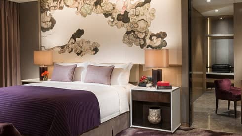 Executive Suite bed, nightstand, lamp under brushstroke mural, purple chair by desk