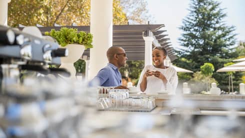 Man and woman drink espresso coffee at bar on sunny patio, white pergola in background