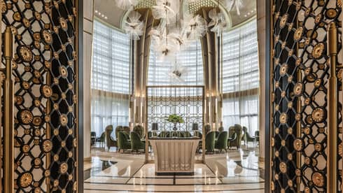 Decorative black-and-brass floral doors open to bright room with green velvet chairs under dome ceiling, modern art 