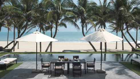 Villa dining table under patio umbrellas by pool, beach and ocean