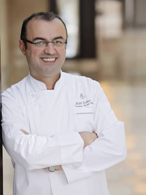 A portrait of Chef Adil Çakıcı leaning against a cream wall