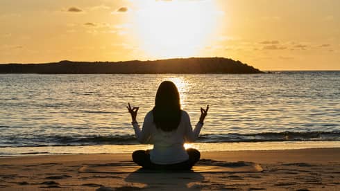 Woman meditates beachside at sunset