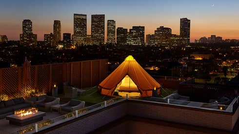 Glowing white tent, bed on rooftop patio by chairs, outdoor fireplace, Beverly Hills sunset city views