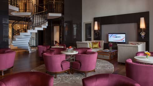 E-Lounge large curved velvet pink chairs around small round tables, modern white spiral staircase in background
