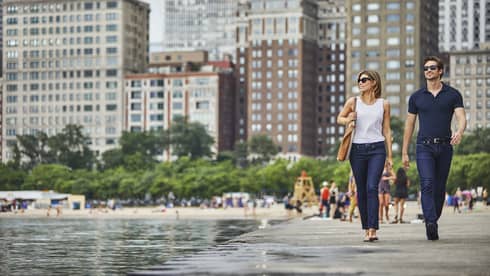 Man and woman wearing T-shirts, jeans and sunglasses stroll along Chicago waterfront