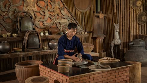 A man in a pottery studio holding a piece of grey clay.