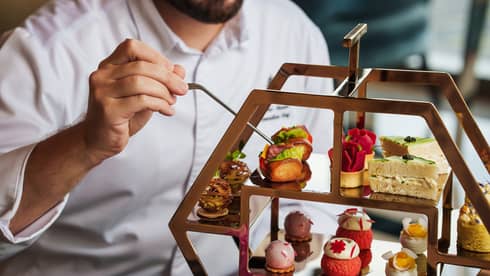 Close up of man with wearing a white button-down shirt organizing pastries on a three-tiered tray for afternoon tea