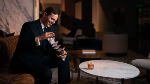 A man in a suit doing playing card drinks while sitting down.