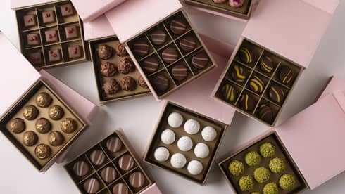 Nine square, pink boxes set on a white background, each open to reveal nine chocolate truffles within, each a different kind