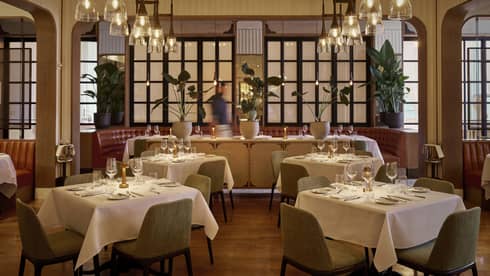 Dining room with dining tables set with tablecloths and glasses, and lights from the ceiling