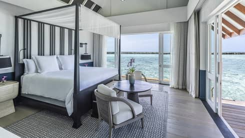 Bedroom with four-poster canopied bed, two-seater round table, double doorway leading to deck with ocean views