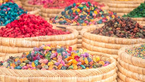 Close-up of multiple round woven baskets bursting with a rainbow of colourful herbs and spices and dried red flowers.