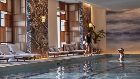 Woman standing on side of pool holding towel, man standing in pool.