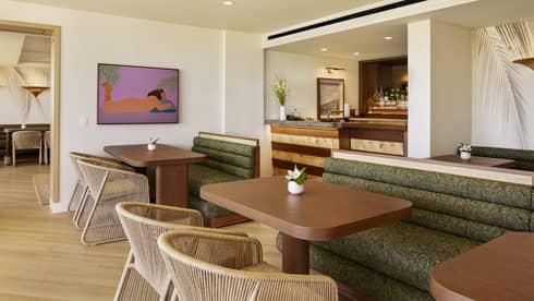 Wooden dining tables in an executive club lounge, featuring large green booths and woven beige chairs