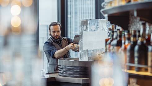 Male bartender shaves ice off a large ice block at luxury hotel bar