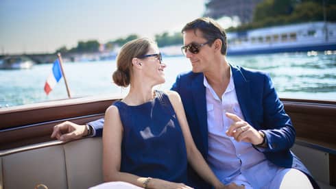Couple enjoy Paris boat ride next to small France flag, Eiffel tower in background