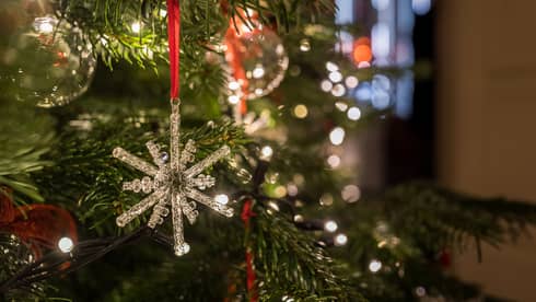 Close-up of a crystal snowflake ornament hanging on a Christmas tree with festive lights in the background
