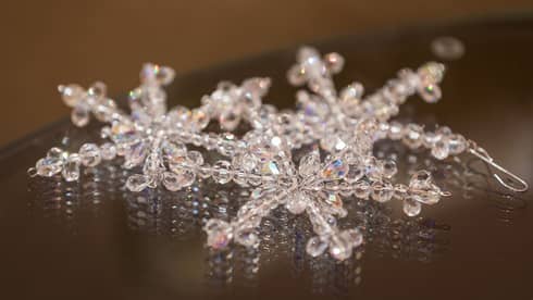 Three snowflake ornaments made of crystal beads placed on a dark table