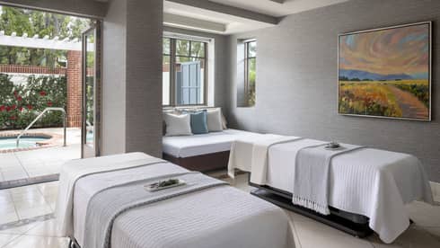 A spa treatment room with two massage beds, a small couch and an open door leading outside.