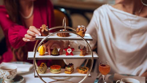 Two guests reach for pastries served on a three-tiered silver tray