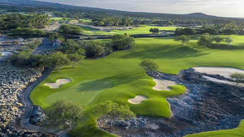 An overhead view of a lush green golf course under a cloudy sky.