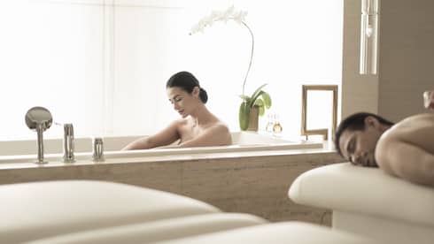 Woman soaks in spa tub near man getting massage 