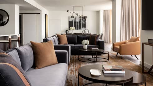 Living room with two grey-blue velvet sofas, tan leather arm chairs, round metal coffee table