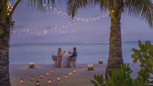 Man and woman dine at table for two alone on decorated beach