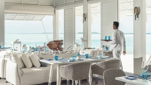 Waiter walks by tables with tray of water glasses at open-air Blu Beach Club
