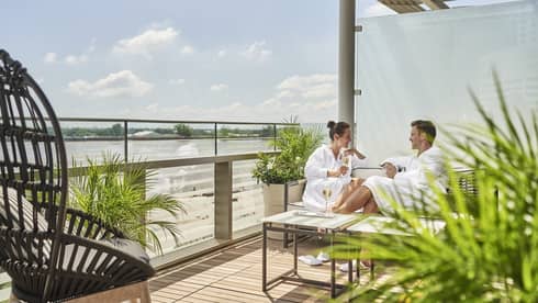 A man and woman in spa robes sitting on a patio with plants.