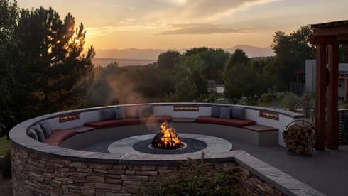 A firepit outside during a sunrise, surrounded by trees and plants.